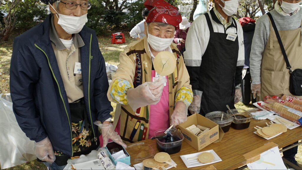 横須賀矯正展に出展した町内会など地域コミュニティ、地域に根差した店舗（コンビニやMAZDAなど）のブースでお菓子を販売する出展者さん