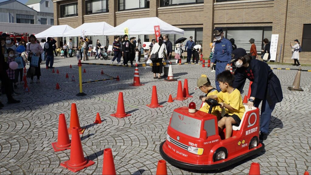 第48回府中刑務所文化祭（2023年開催）の体験コーナー消防車のミニカーに乗る子どもたち