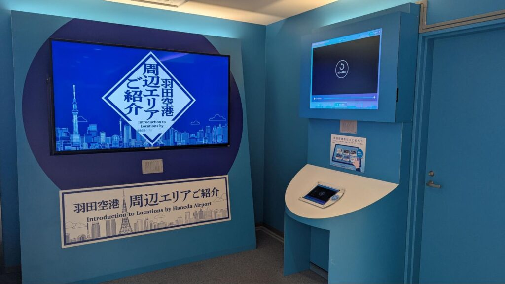 羽田空港の「周辺エリアご紹介」情報コーナー。大型モニターに東京スカイツリーや都心のビル群が映し出され、観光案内や周辺情報を紹介している。