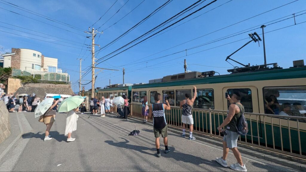 鎌倉の海岸線を走る、江ノ島電鉄（江ノ電）とスラムダンクの聖地巡礼をする海外の観光客