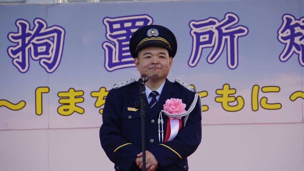 制服を着た内山信二氏がステージ上で挨拶をしている様子