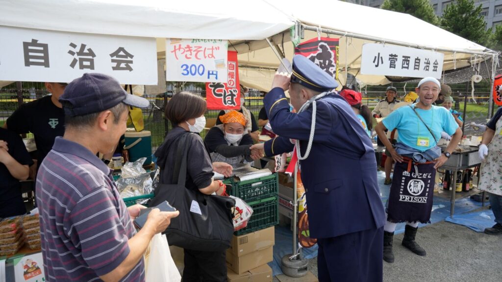 自治会の屋台の販売スタッフと、内山信二氏が握手を交わしている様子