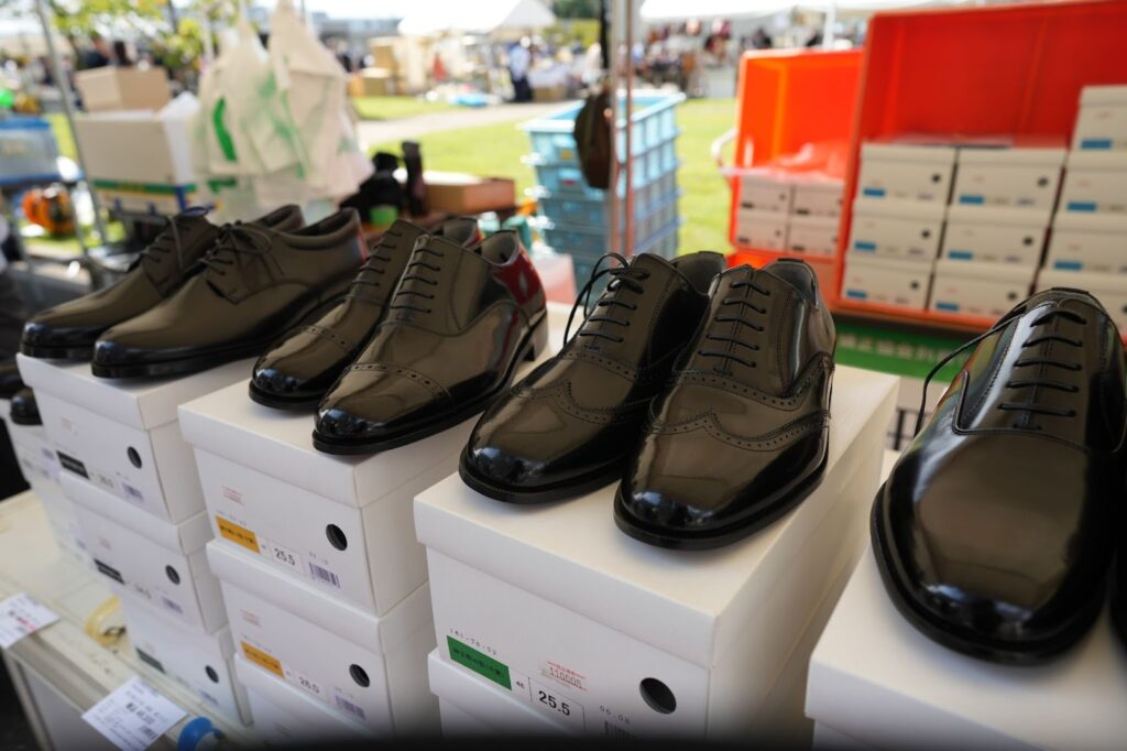 白い靴箱の上に並べられた黒の革靴が展示されている様子
