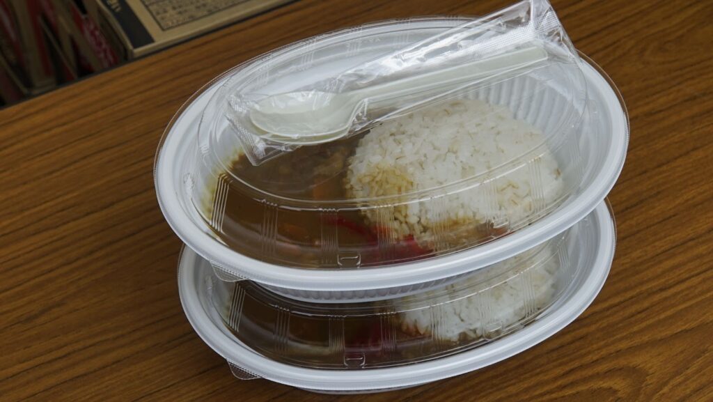 透明のフタが付いた容器に盛り付けられたカレーライスのテイクアウトパック