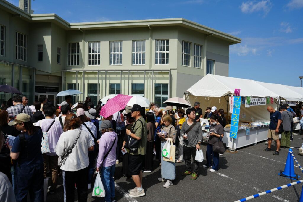 建物前に設置されたテントで、来場者が列を作って並んでいる様子