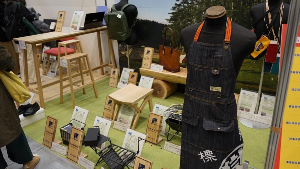 新製品展示ブースに並ぶマル獄エプロンや鞄などの商品